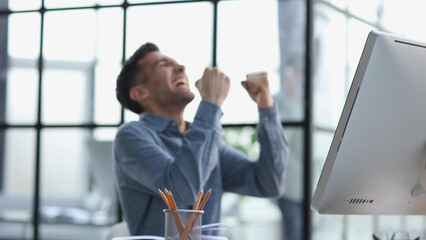 Happy businessman rejoices at success in the workplace in the office, looks up with a euphoric expression on his face.