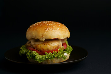Close-up of a delicious fresh homemade burger with lettuce, cheese, onion and tomato on a rustic wooden board on a dark background