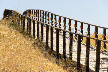 Fototapeta premium Wooden fence bridge over meadow and grass. Made of rope ropes. Sidewalk pathway