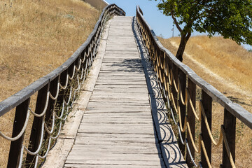 Obraz premium Wooden fence bridge over meadow and grass. Made of rope ropes. Sidewalk pathway