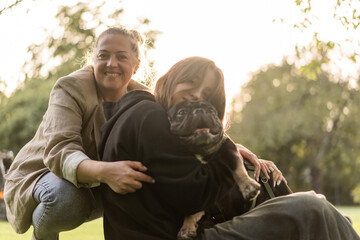 A young teenage girl with her mother hugs her French bulldog 