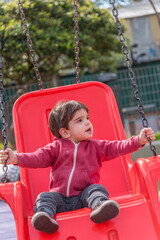 Little kid having fun swinging at the playground in the park.