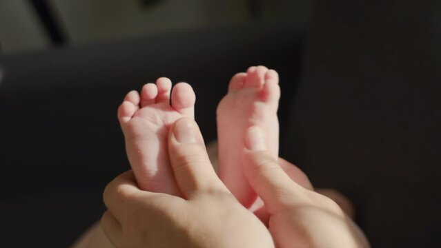 Close up of masseur massaging little baby foot lying on sofa. Unknown loving mother massaging baby finger feet. Caring mom doing massaging infant boy at home. Newborn child about 4-6 months old