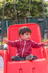 Little boy swinging on the swing at the playground in the park.