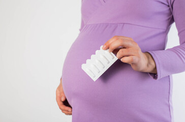 A pregnant girl in a lilac blouse holds rectal suppository against the background of her belly. The...