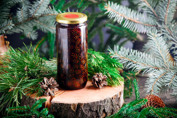 Jam from young pine cones in syrup on a background with pine branches