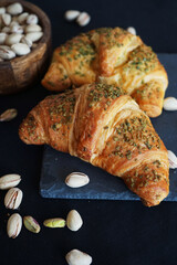 Pistachio croissants next to a plate with whole pistachios on a dark background