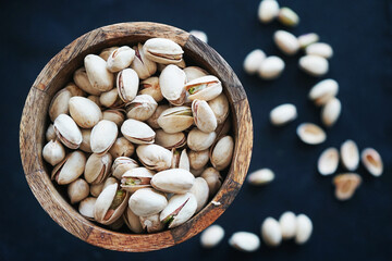 Pistachios in a wooden bowl and on a black tablecloth