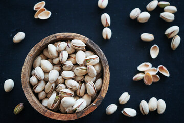 Pistachios in a wooden bowl and on a black tablecloth