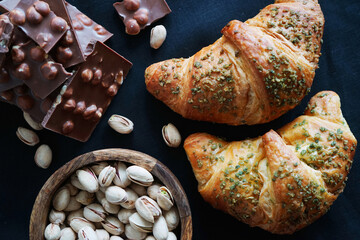 Croissants, pistachios and chocolate slices on a dark background