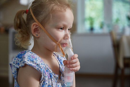 Sick little girl making inhalation with nebulizer to reduce coughing. Bronchitis and asthma treatments for children.