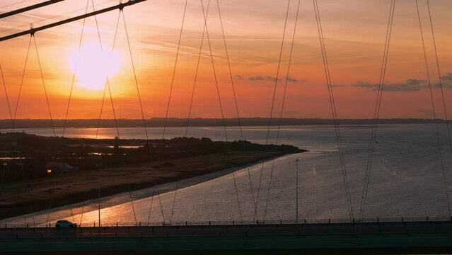 Fly above the Humber Bridge in an aerial drone video at sunset, where cars paint a tranquil picture