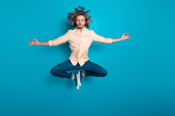 Obraz premium Full size photo of peaceful man with long hairstyle dressed yellow shirt levitating while meditating isolated on blue color background