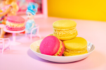 Blurred dolls drinking tea with macarons. Selective focus on macarons