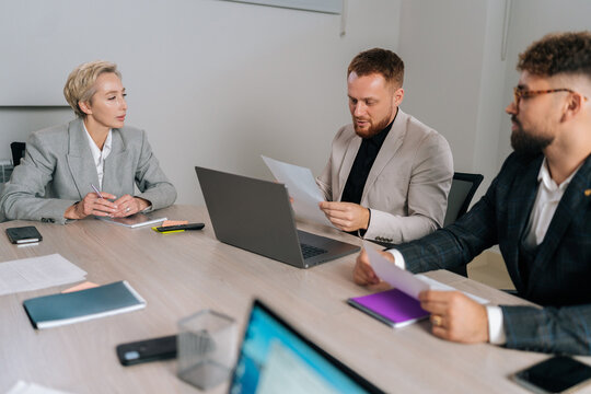 Focused Middle-aged Female Team Leader Sitting At Table With Diverse Ages Colleagues, Discussing Working Issues At Negotiations Meeting. Skilled Employees Developing Startup Marketing Strategy.