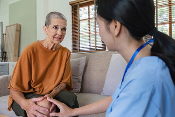 A sick old woman with a leg injury on the sofa receive help from a young nurse on a home visit.