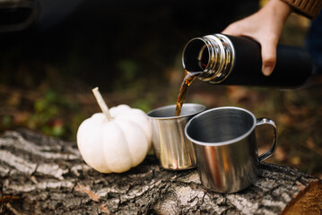 A hand holding a thermos and pouring hot tea into metal cups