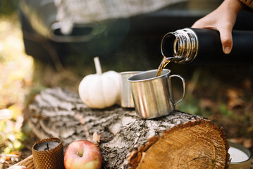 A metal cup on a wooden log into which hot tea or coffee is poured from a thermos