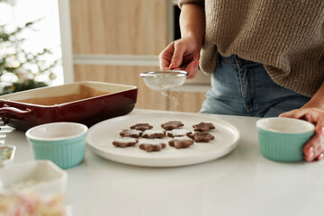 Unrecognizable woman decorating Christmas cookies with a icing sugar