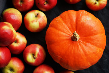 Orange pumpkin next to ripe apples on a dark background