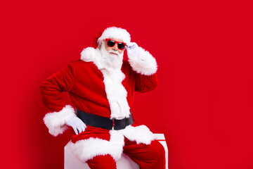 Photo of funky nice senior man santa claus dressed traditional new year clothes sitting empty space isolated on red color background