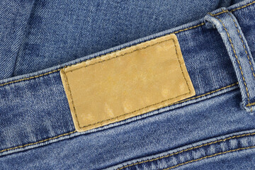 Brown rectangular background in the center of a blue denim background. Blank tag on jeans