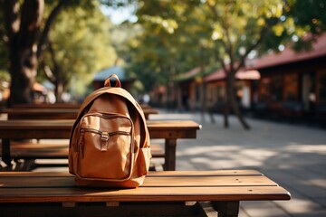 Brown backpack on the wooden table in the school park. Autumn background.