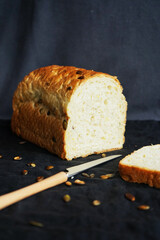 Fresh white bread with pumpkin seeds next to a knife on a dark background