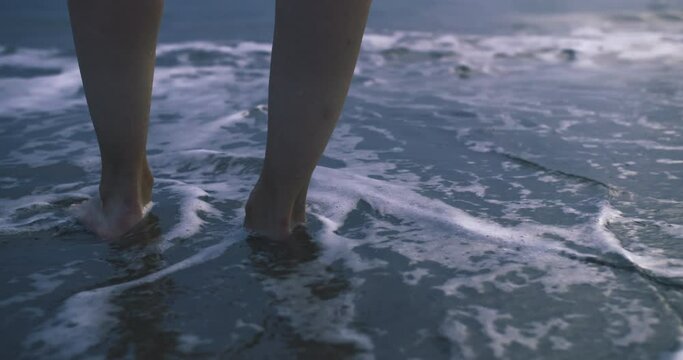 Close-up of woman legs in sea wave foam on beach, low angle view