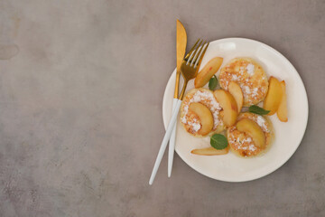 Cottage cheese pancakes with peach and mint leaves on a white plate on a grey background.