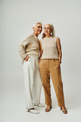 full length of joyful female friends standing with hands in pockets on grey, fashionable aging