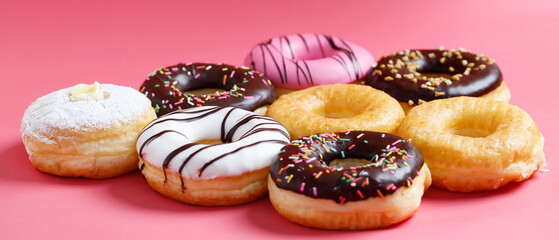 assorted donuts with chocolate frosting, topping sprinkles donuts Colorful variety and Variety of flavors mix of multi colored sweet donuts with frosted sprinkled on pink background. top view