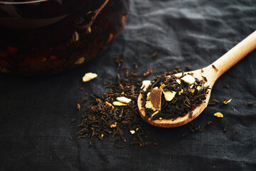 Black tea with pieces of fruit on a wooden spoon next to the teapot on a dark background