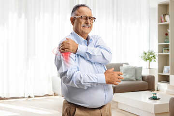 Mature man suffering from arthritis in the shoulder joint holding red spot - obrazy, fototapety, plakaty