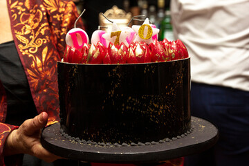 Bolo de aniversário de cor vermelha e preta com velas acesas.
