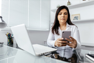 Businesswoman using laptop and smart phone at desk