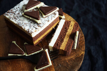 Chocolate cake next to pieces of chocolate on a wooden stand on a dark background
