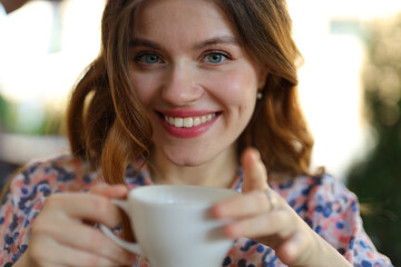 A happy young woman enjoying a hot cup of coffee in a cafe, her cheerful smile radiating morning relaxation.