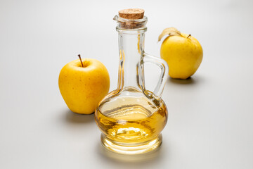 Apple cider vinegar in a glass bottle and fresh yellow apples.