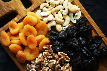 Dried apricots, prunes, nuts on a wooden board with horns on a dark background