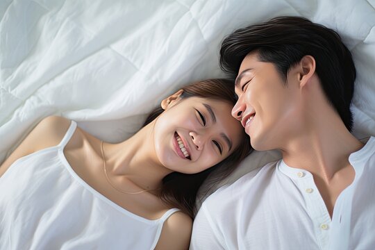 lovely asian couple on bed peacefully sleeping looking at each other and smiling