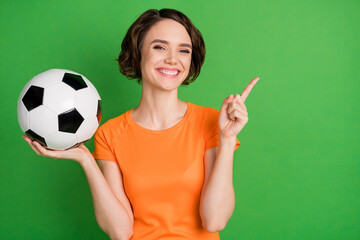 Portrait of cheerful girl hold ball indicate finger empty space feedback offer isolated on green...