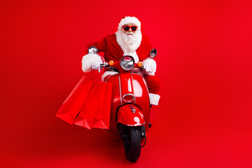 Portrait of excited cool santa claus with white beard in sunglass driving scooter with shopping...