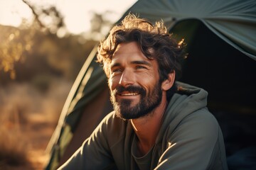Fototapeta premium Portrait of man looking at camera while near camping tent at sunset
