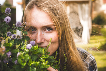 Smiling woman smelling mint in her garden. Love for plants. - obrazy, fototapety, plakaty