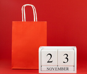 November 23 white wooden calendar and paper bag on a red background close-up. Concept trade, store,...