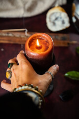 hand of a woman with jewels holding a lighted candle during a fortune telling session