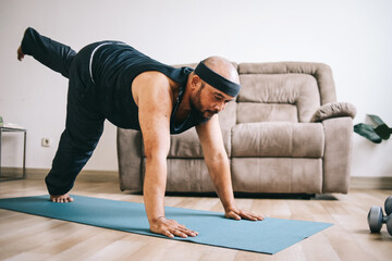 Funny fat bearded man in sportswear doing yoga or workout at home