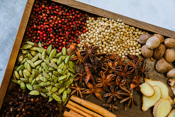 Cinnamon, clove, star anise, cardamom, juniper, nutmeg, ginger and pepper whole spices on a wooden tray