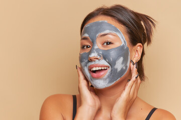 Cute girl doing cosmetic procedures, made clay mask on her face, looks at the camera with smile, skin care routine concept, copy space